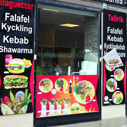 Restaurangskylt med svart, röd och orange bakgrund. Bilder på olika maträtter som hamburgare och kebab. Rätternas namn står med vitt.